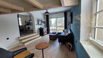 Ein großzügiger Wohnbereich mit einer Couch, einem Couchtisch und einem Fernseher. Eine Treppe führt zu einer anderen Ebene, und ein Fenster bietet einen Blick ins Freie.