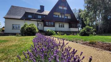 Ein zweistöckiges Haus mit geneigtem Dach, einem Lavendelgarten und einem Kiesweg.