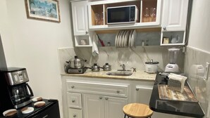 Een compacte keuken met witte kastjes, een zwarte koffiezetapparaat, een magnetron en een blender.