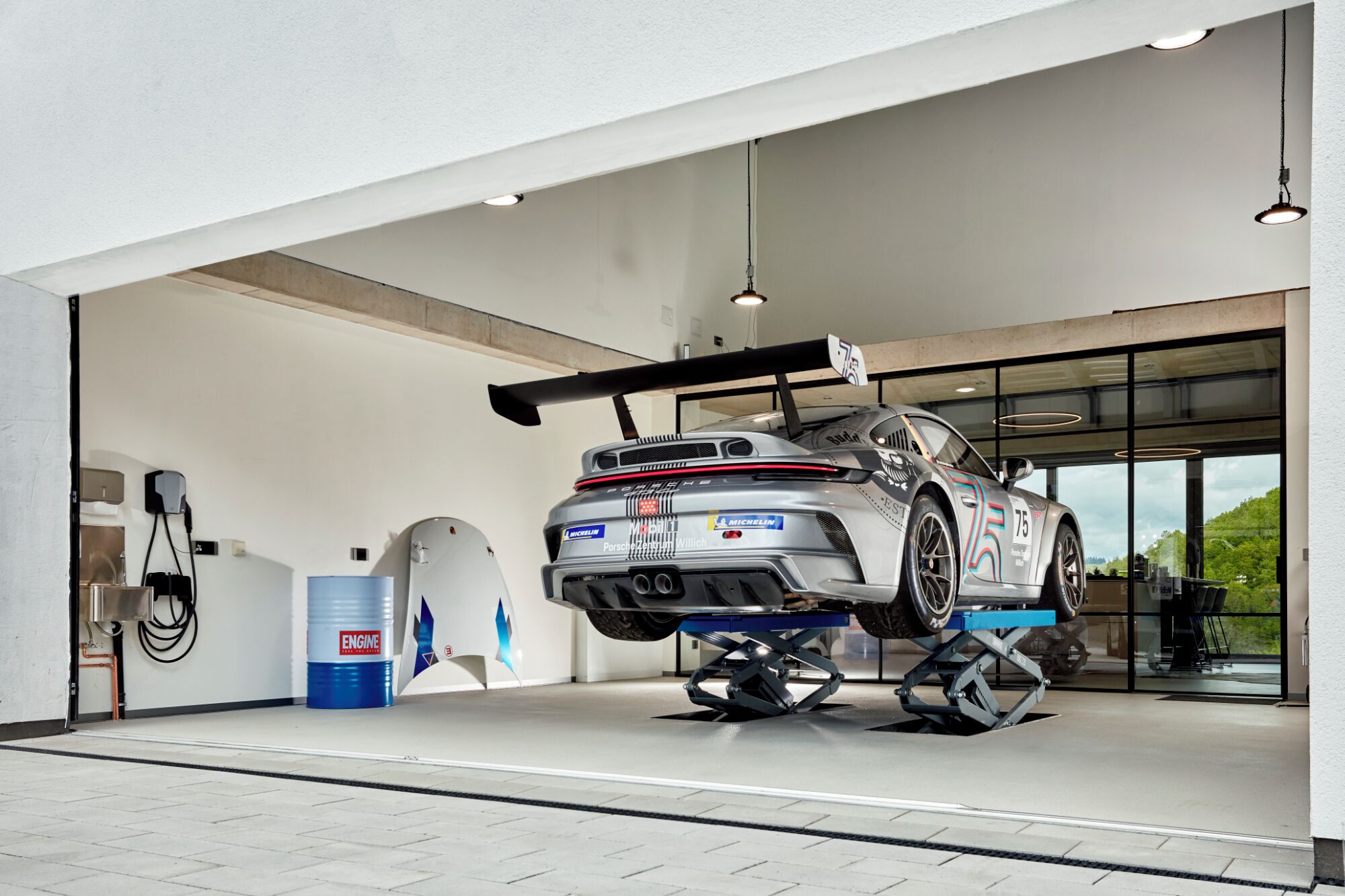 A car elevated on a lift in a garage with a large window and a view of greenery outside.