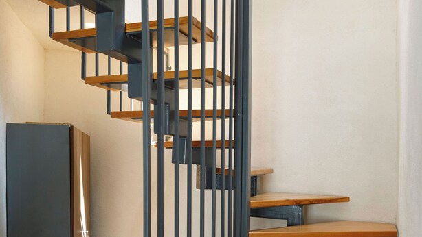 Una escalera de caracol con escalones de madera y barandillas de metal negro.
