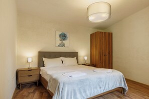 Ein ordentlich eingerichtetes Schlafzimmer mit einem Bett, Nachttischen, einem Holzschrank und einem Bild an der Wand.