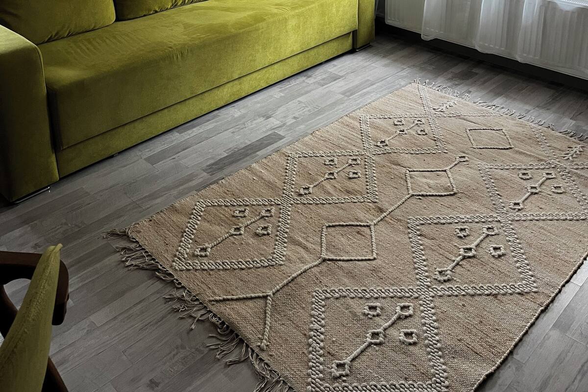 Un salón con un sofá verde, un tapete estampado y cortinas de encaje.