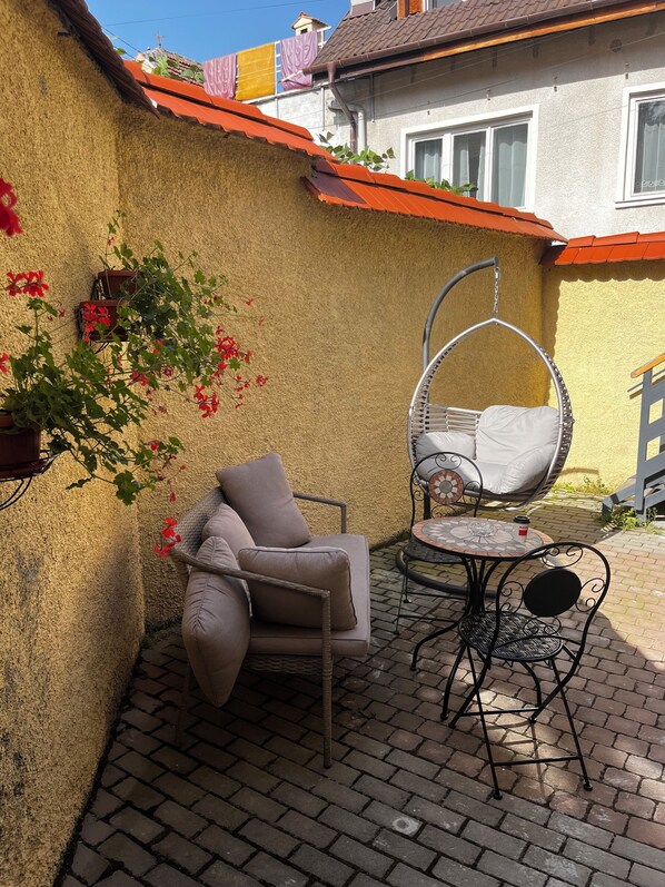 Eine Terrasse mit einem Korbstuhl, einem gepolsterten Sessel und einem kleinen Tisch.