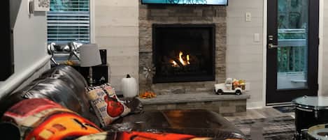 A living room with a fireplace, a television mounted above it, and a sofa with decorative pillows.