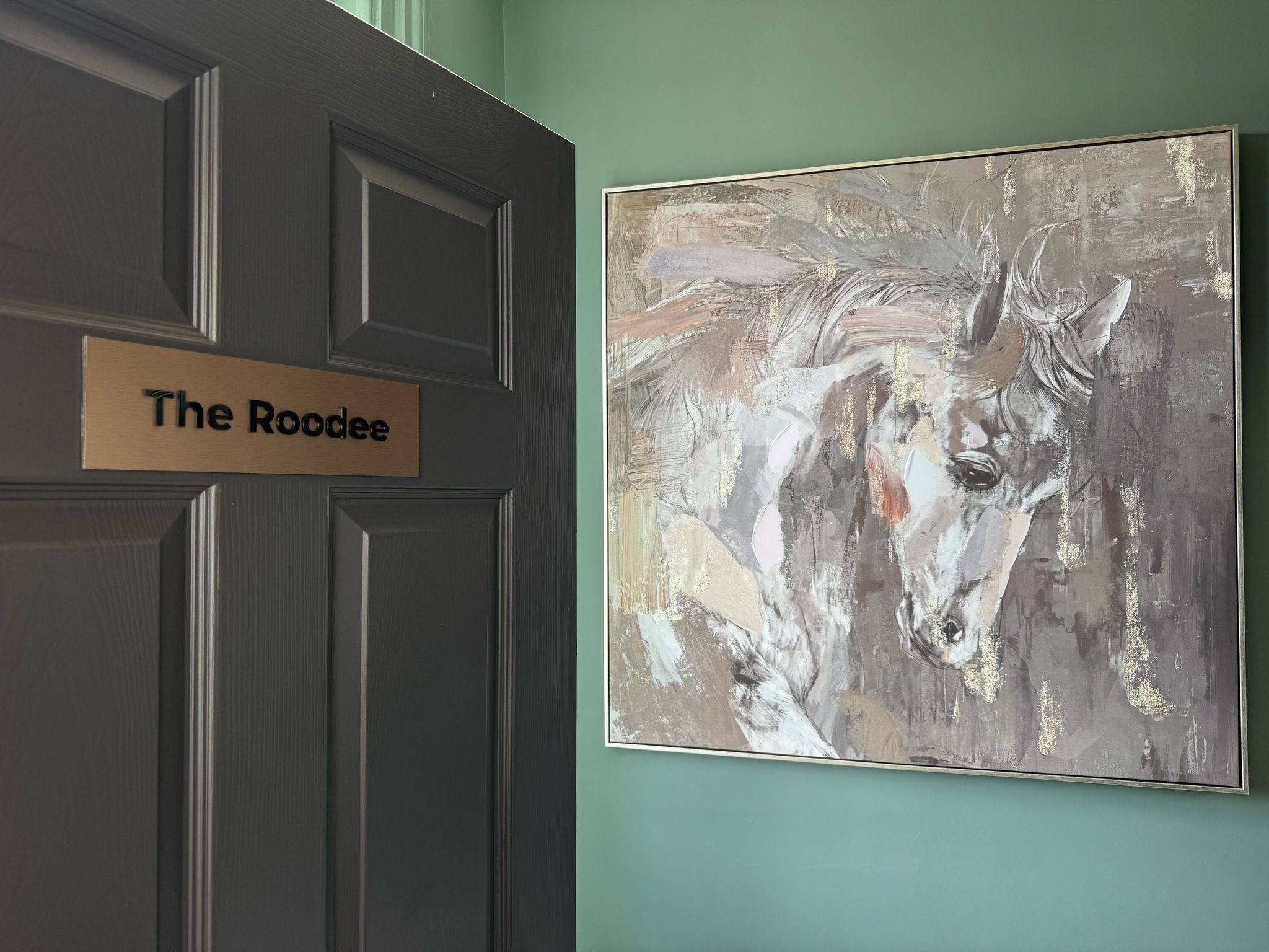A door with a sign reading 'The Roodee' and a large abstract painting on the wall.