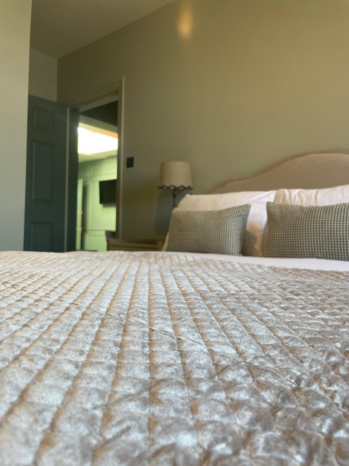 A bed with a textured blanket, a lamp, and a door leading to another room.