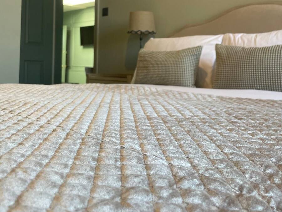 Una cama con un edredón texturizado, una lámpara y una puerta que da a otra habitación.