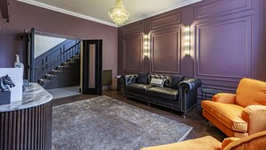 A modern living room with a dark leather sofa, a bright orange armchair, a marble reception desk, and a chandelier. - The Seven (Chester)