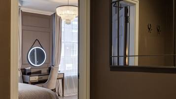 A hotel room with a bed, a vanity with a mirror, a desk, and a chandelier.