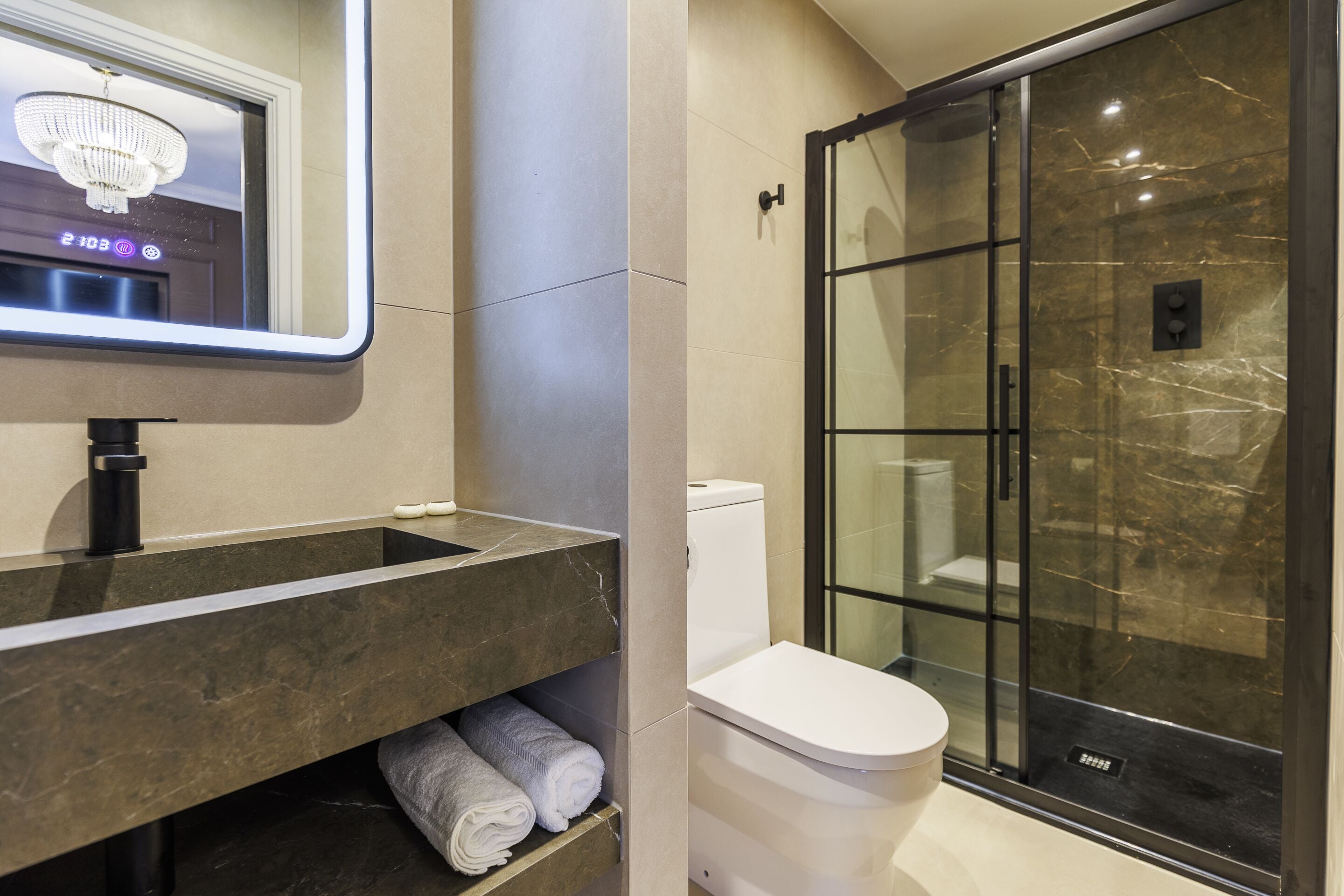 A modern bathroom with a marble sink, a toilet, and a glass-enclosed shower.