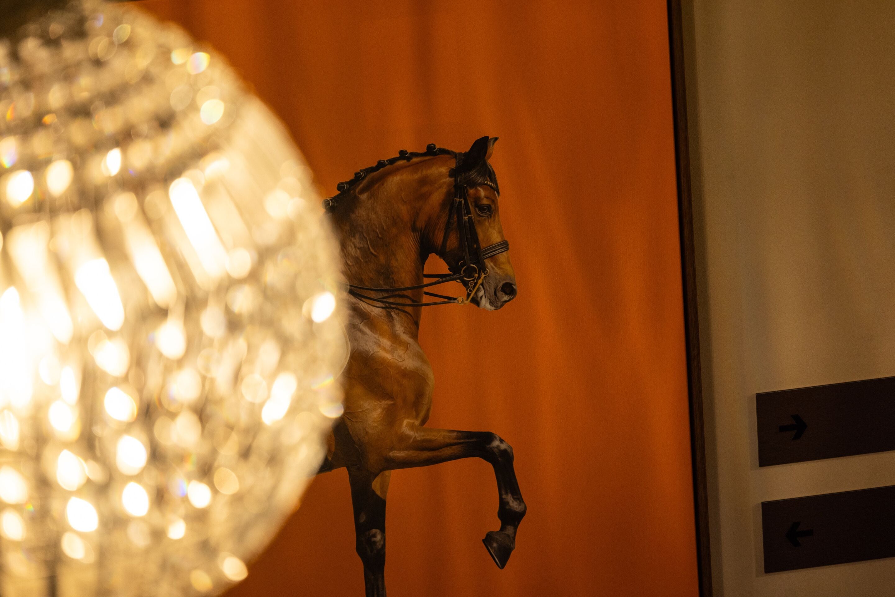 A statue of a horse in a room with an orange wall and directional signs.