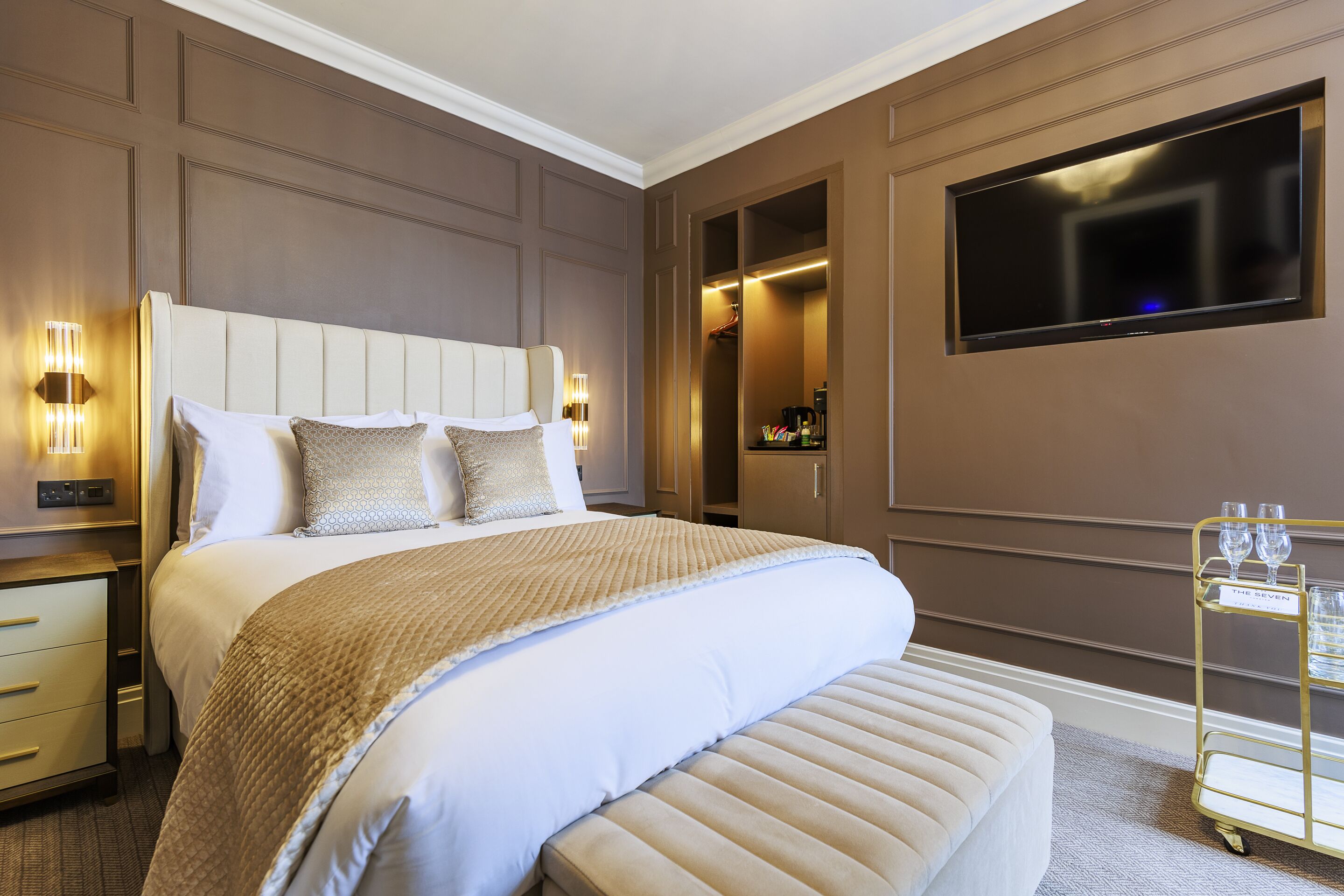 A hotel room with a large bed, bedside lamps, a TV, and a minibar.