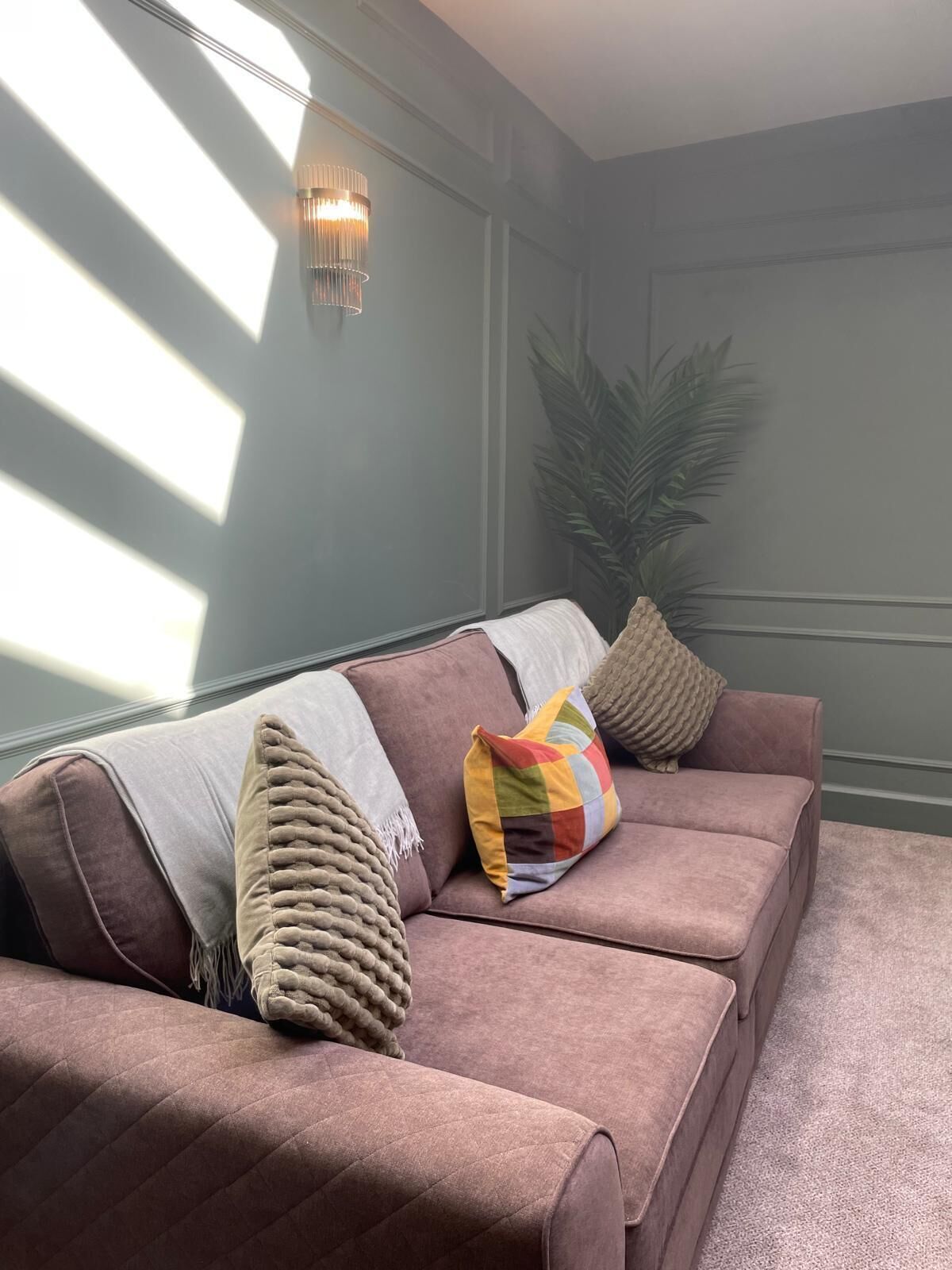 A modern living room with a sofa, decorative pillows, a plant, and a wall-mounted light fixture.