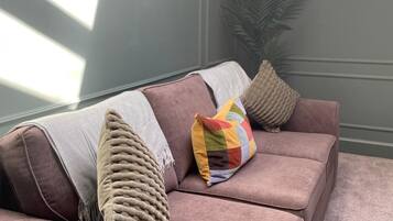 A modern living room with a sofa, decorative pillows, a plant, and a wall-mounted light fixture.