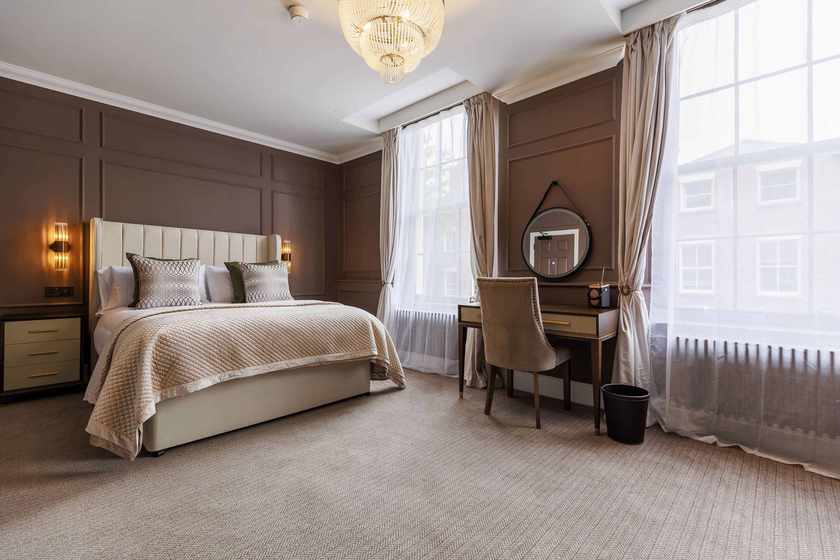 A hotel room with a bed, a desk, a chair, a mirror, and a window with curtains.