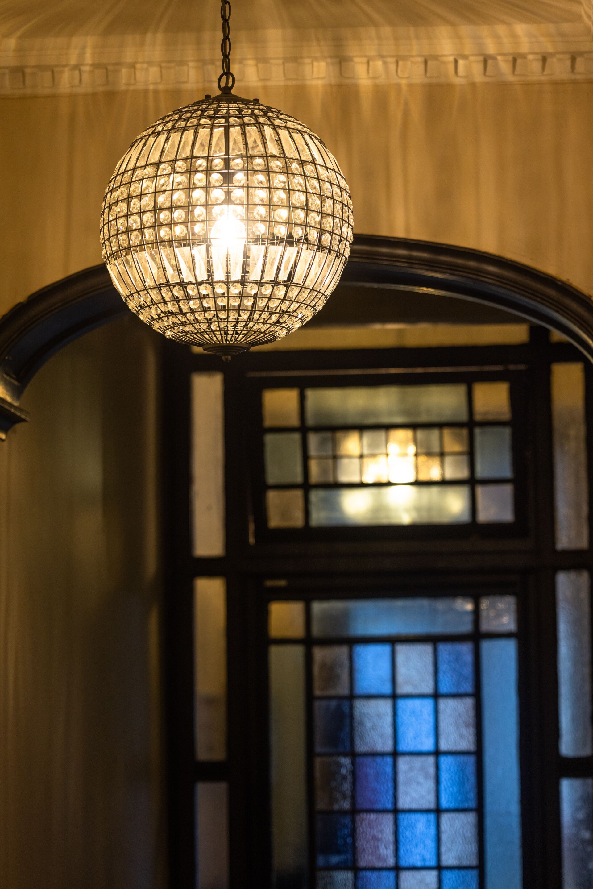 Un candelabro de cristal colgante en una habitación con un arco oscuro y una ventana con paneles de vidrio esmerilado.