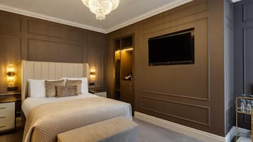 Et hotelværelse med en stor seng, sengeborde med lamper, en lysekrone, et fjernsyn og et minibar.