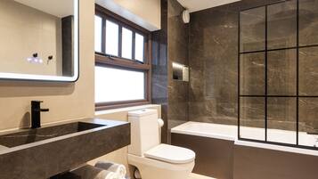 A modern bathroom with a large mirror, a bathtub, a toilet, and a vanity with a sink.