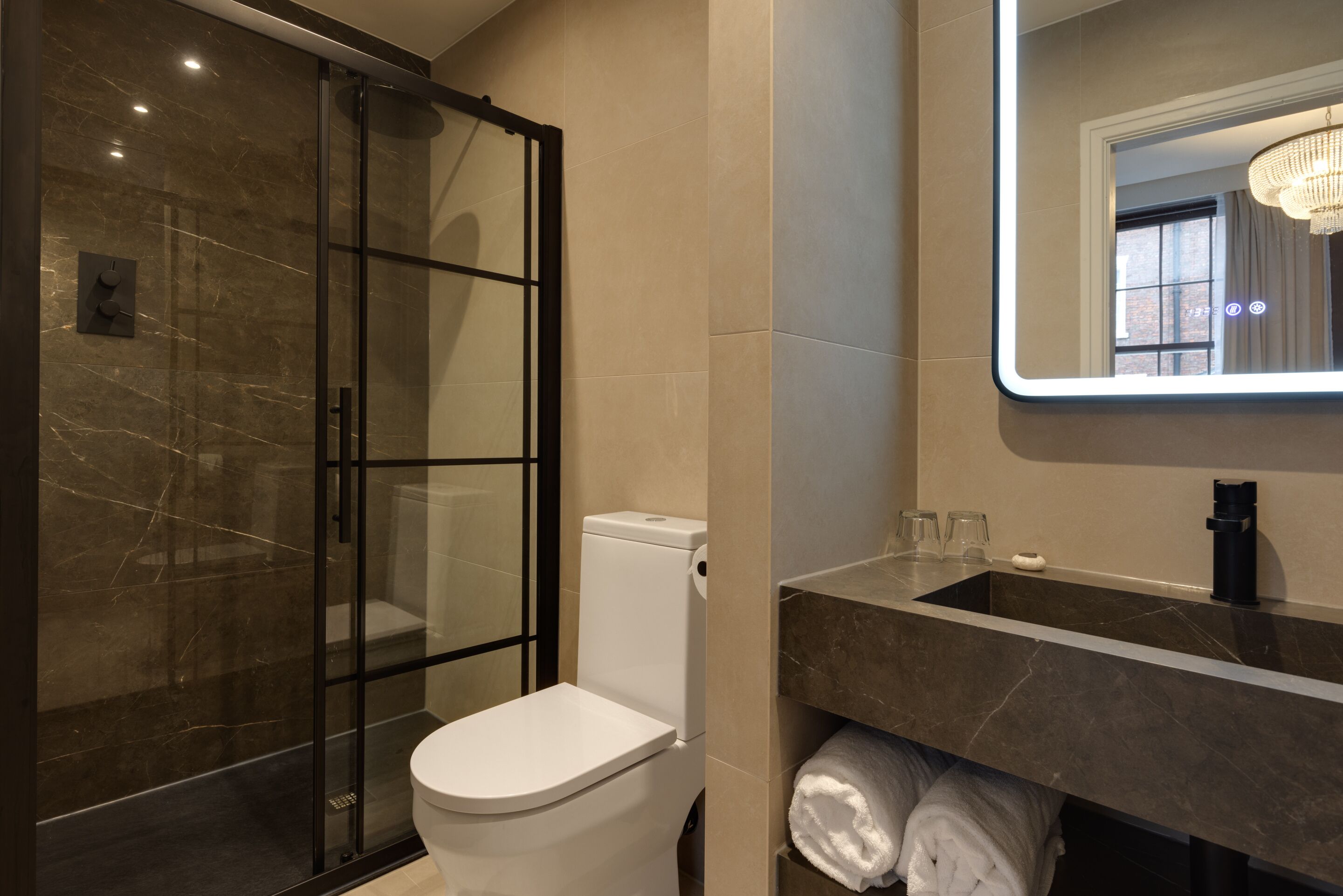 A modern bathroom with a glass-enclosed shower, a white toilet, a sink with a mirror, and towels on a shelf.