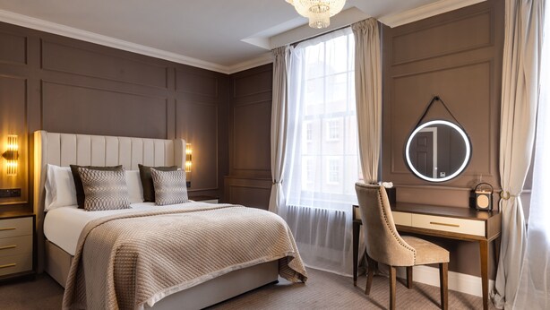 A bedroom with a bed, bedside table, lamp, desk, chair, and a round mirror. - The Seven (Chester)