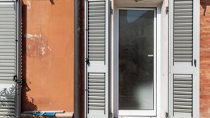 Une terrasse carrelée avec une grille métallique, une porte à volets et des unités de climatisation fixées à un mur de briques.