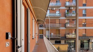 Un couloir doté d’un sol carrelé, d’une rambarde en métal et de portes donnant accès aux appartements.