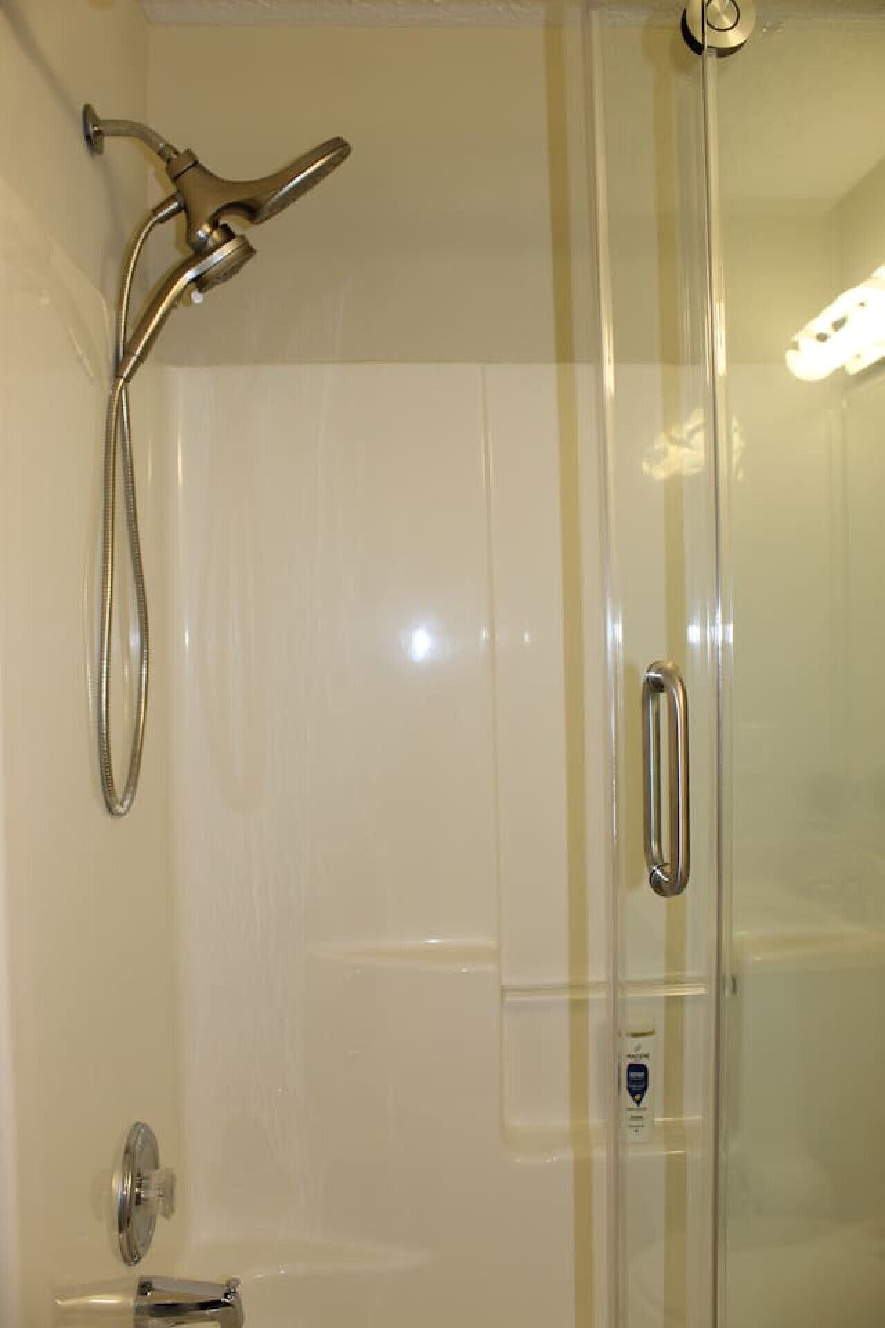 A glass-enclosed shower with a handheld showerhead and a wall-mounted faucet.
