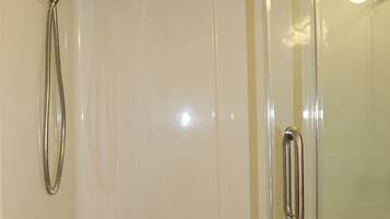 A glass-enclosed shower with a handheld showerhead and a wall-mounted faucet.