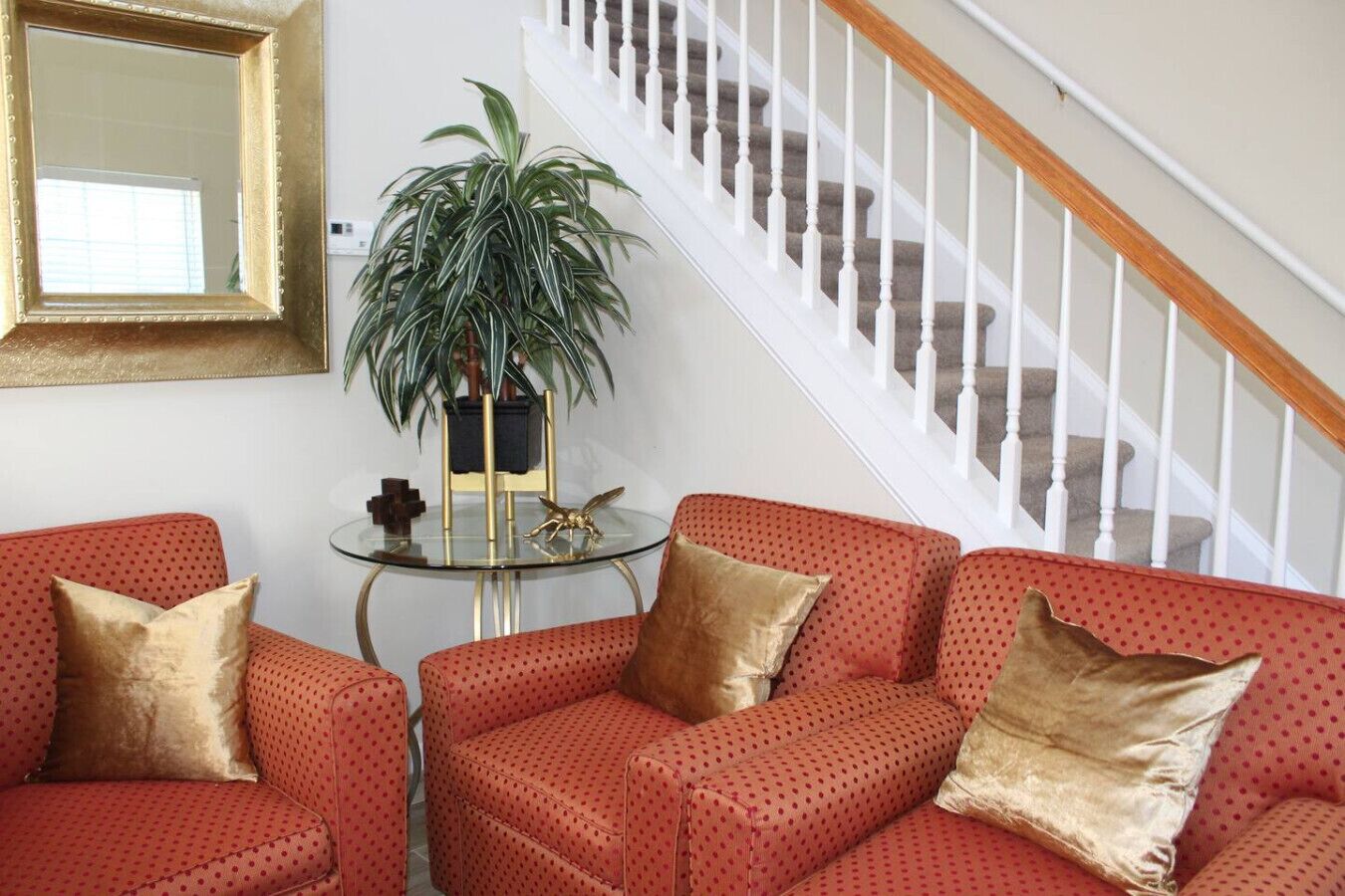 A living room with a red sofa set, a glass coffee table, and a staircase with white railings.