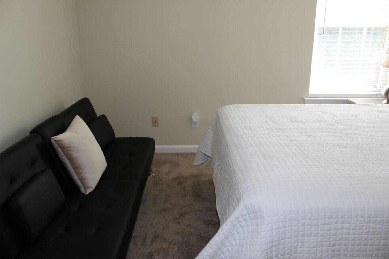 Une chambre à coucher avec un canapé noir, un lit blanc et une fenêtre avec des stores.