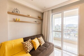 A modern living room with a brown sofa, yellow cushions, and a city view through large windows.