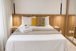 Une chambre d’hôtel comprenant un lit, deux tables de chevet, une commode, un miroir et une fenêtre avec des rideaux.