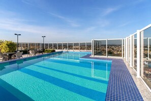 A rooftop infinity pool with clear blue water, surrounded by glass railings and outdoor seating.