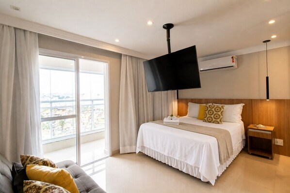 A hotel room with a bed, a TV, a bedside table, a nightstand, and a sofa.