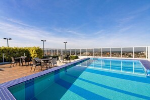 A rooftop pool with a clear view of the cityscape, surrounded by outdoor seating and a glass enclosure.