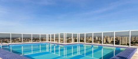 Piscina en la azotea con vistas a la ciudad, rodeada de barandillas de vidrio.