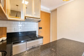 Une cuisine avec un plan de travail noir, des carreaux blancs, une hotte en acier inoxydable et une porte en bois.