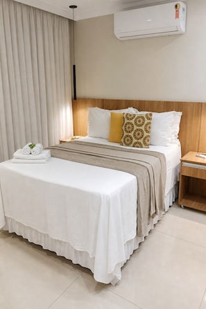 A hotel room with a bed, bedside table, and an air conditioning unit.