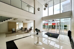 A spacious lobby with a central table, seating area, and a staircase leading to an upper level.
