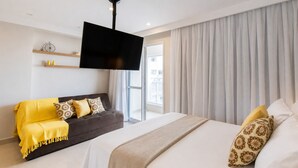 Ein modernes Hotelzimmer mit einem großen Bett, einer Couch, einem flachbildfernseher an der Wand und einem großen Fenster mit Vorhängen.