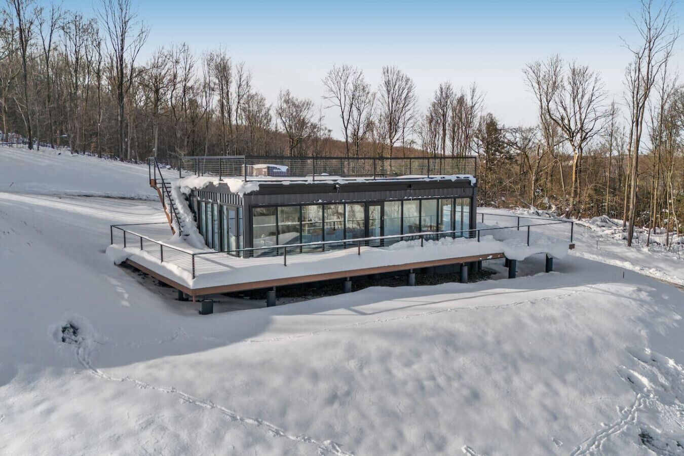 Un bâtiment moderne en verre, doté d’un toit plat, entouré d’un paysage enneigé et d’arbres.