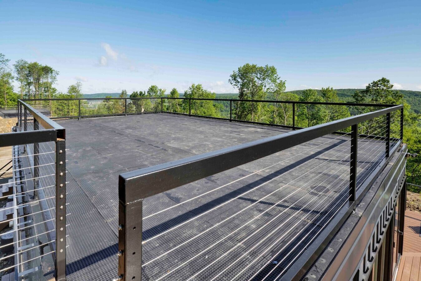 Terraza en la azotea con barandilla de metal, con vistas a un paisaje boscoso.