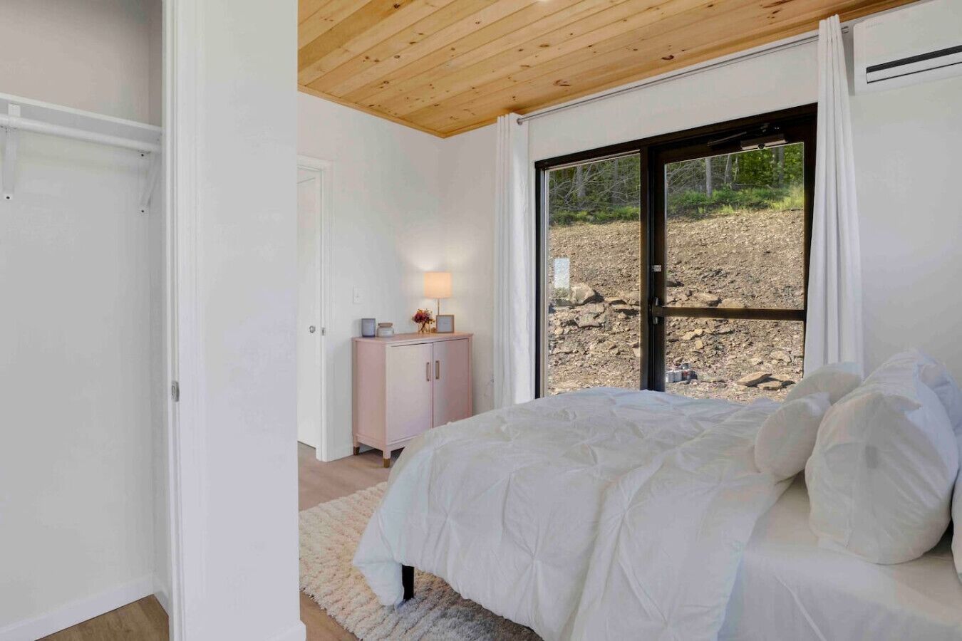 Un dormitorio con una cama grande, una mesita de noche, un aparador y una ventana con vistas a un paisaje rocoso.