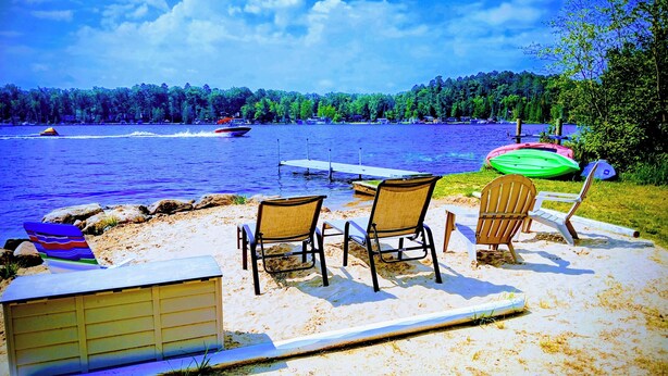 Terraza junto al lago con sillas de playa, un bote y un muelle.