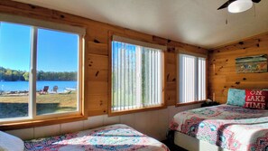 Une cabane avec deux lits, de grandes fenêtres et une vue sur un lac.