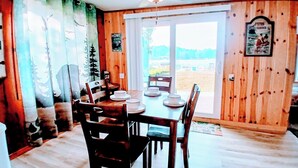 Comedor con mesa y sillas de madera, ventilador de techo y vista al exterior a través de un ventanal corredizo.