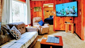 Interior acogedor de una cabaña con sofá, sillón y televisor montado en la pared.