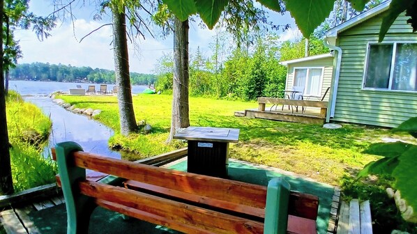 Un banco de madera junto a un río, con una casa al fondo.