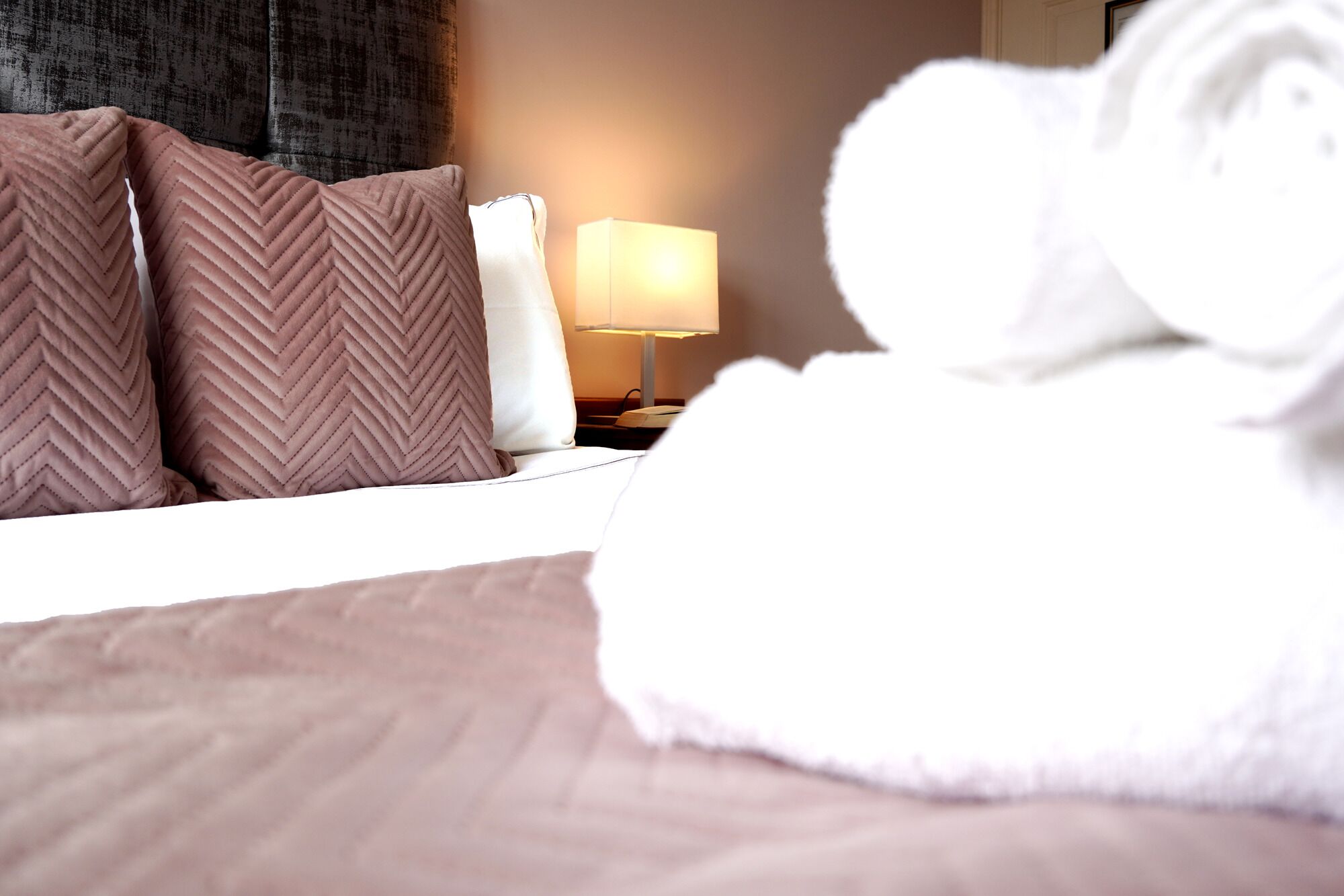 Habitación de hotel con una cama, almohadas, una lámpara y una toalla enrollada.